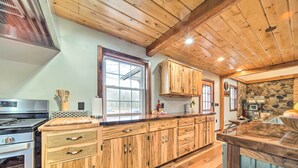 A kitchen with wooden cabinets, a large island, a stove, and a stone wall.