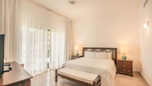 A hotel room with a large bed, a bench, a desk, and two bedside tables with lamps. - Apartment for 5 with Balcony and Jacuzzi Oasis (Las Terrenas)