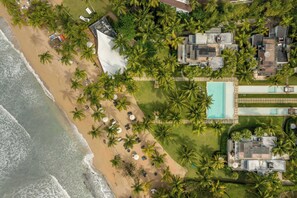 An aerial view of a beachfront property with a swimming pool, palm trees, and multiple buildings.