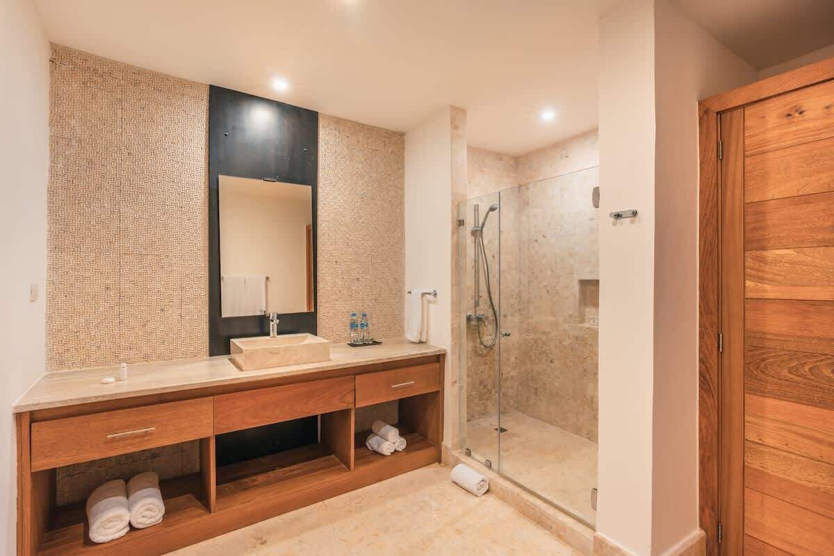 A modern bathroom with a large mirror, two sinks, a shower, and wooden cabinetry.