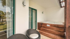A modern bathroom with a wooden bathtub, a glass shower enclosure, and wicker chairs. - Apartment for 5 with Balcony and Jacuzzi Oasis (Las Terrenas)