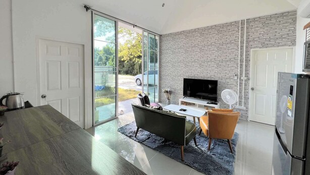 A modern kitchen with a large island, a flat-screen TV, and a dining area with a sofa and chairs. - Homerent @ Sariam Lake Chiang Mai (San Pa Thong)
