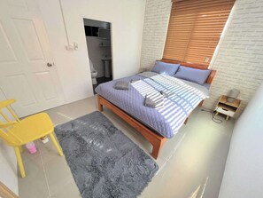 A bedroom with a bed, a chair, a rug, a window with blinds, and a small shelf.