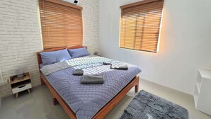 A bedroom with a bed, two windows with blinds, a white brick wall, and a small bedside table. - Homerent @ Sariam Lake Chiang Mai (San Pa Thong)