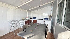 A modern kitchen with white cabinets, a built-in oven, and a dining area with a grey table and chairs. - Homerent @ Sariam Lake Chiang Mai (San Pa Thong)