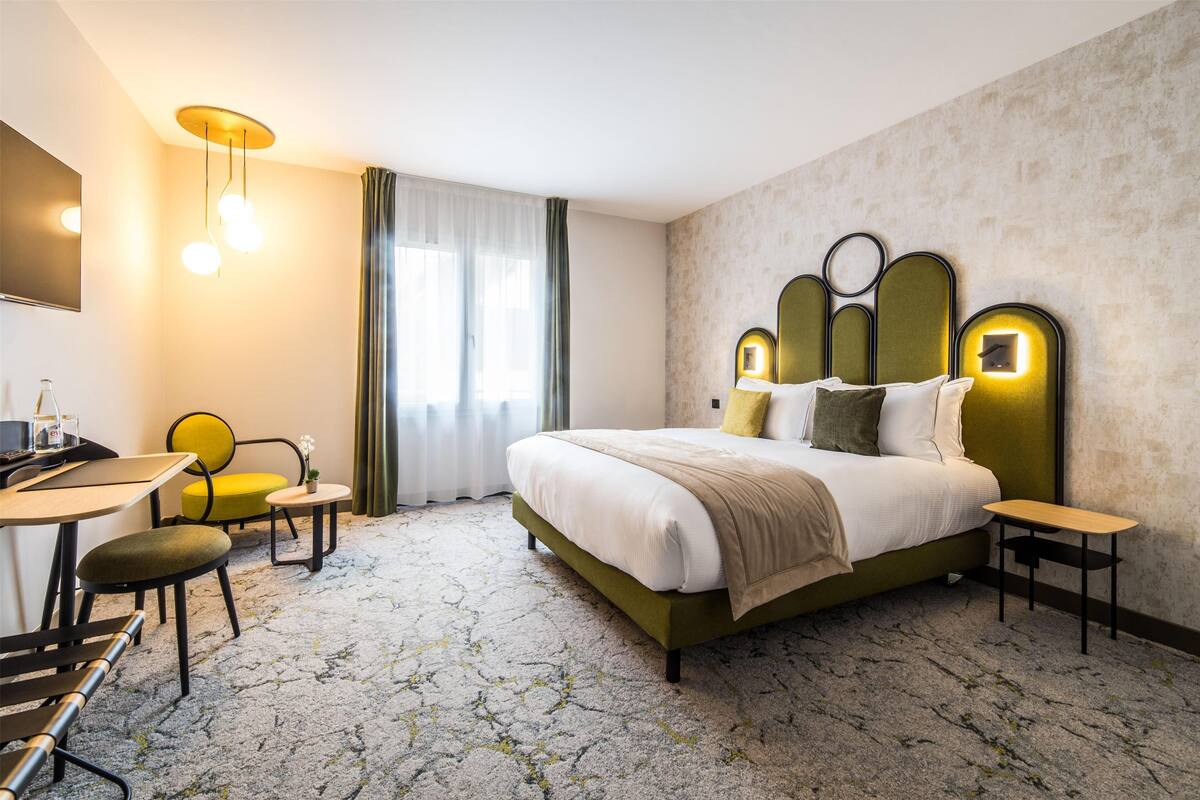 Ein Hotelzimmer mit einem großen Bett, einem Schreibtisch, einem Stuhl und einem kleinen Tisch.