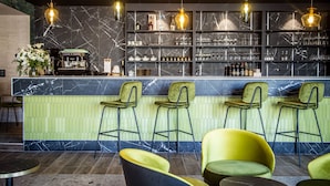A bar area with a marble countertop, green bar stools, and overhead pendant lighting.