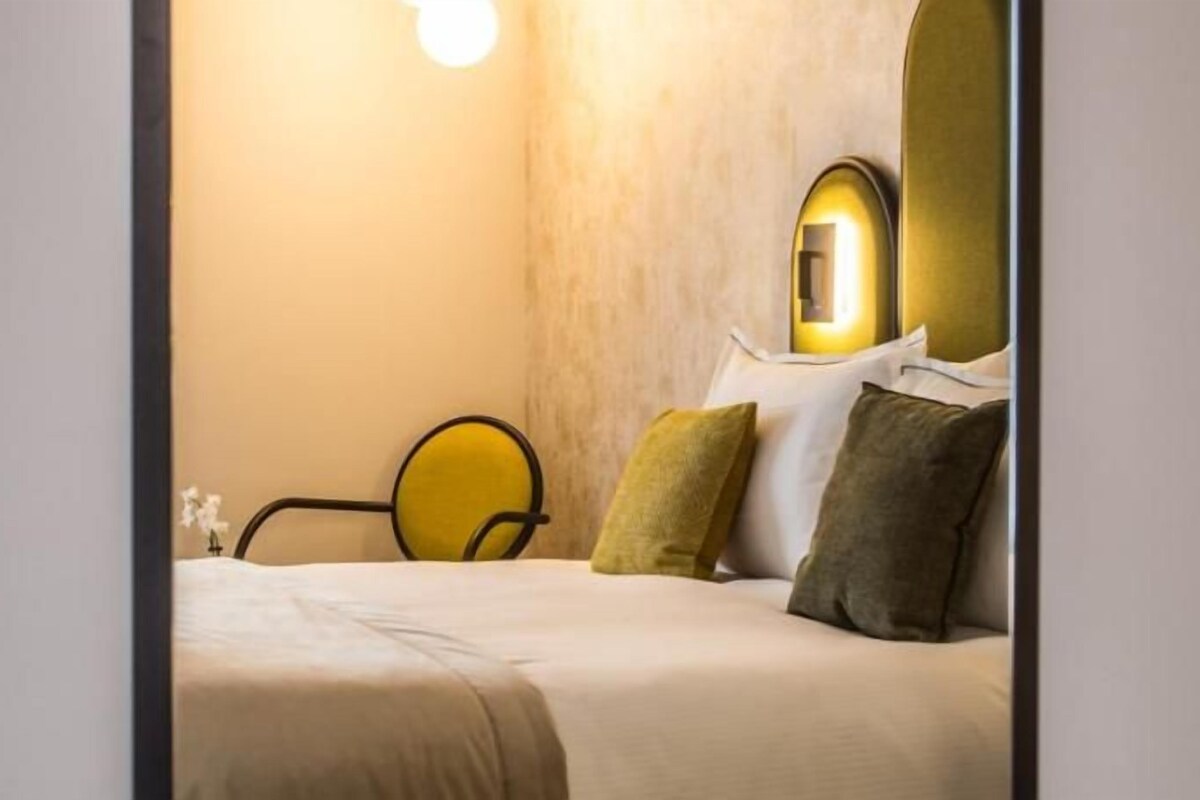 A neatly made bed with pillows, a bedside table, and a wall-mounted light fixture.