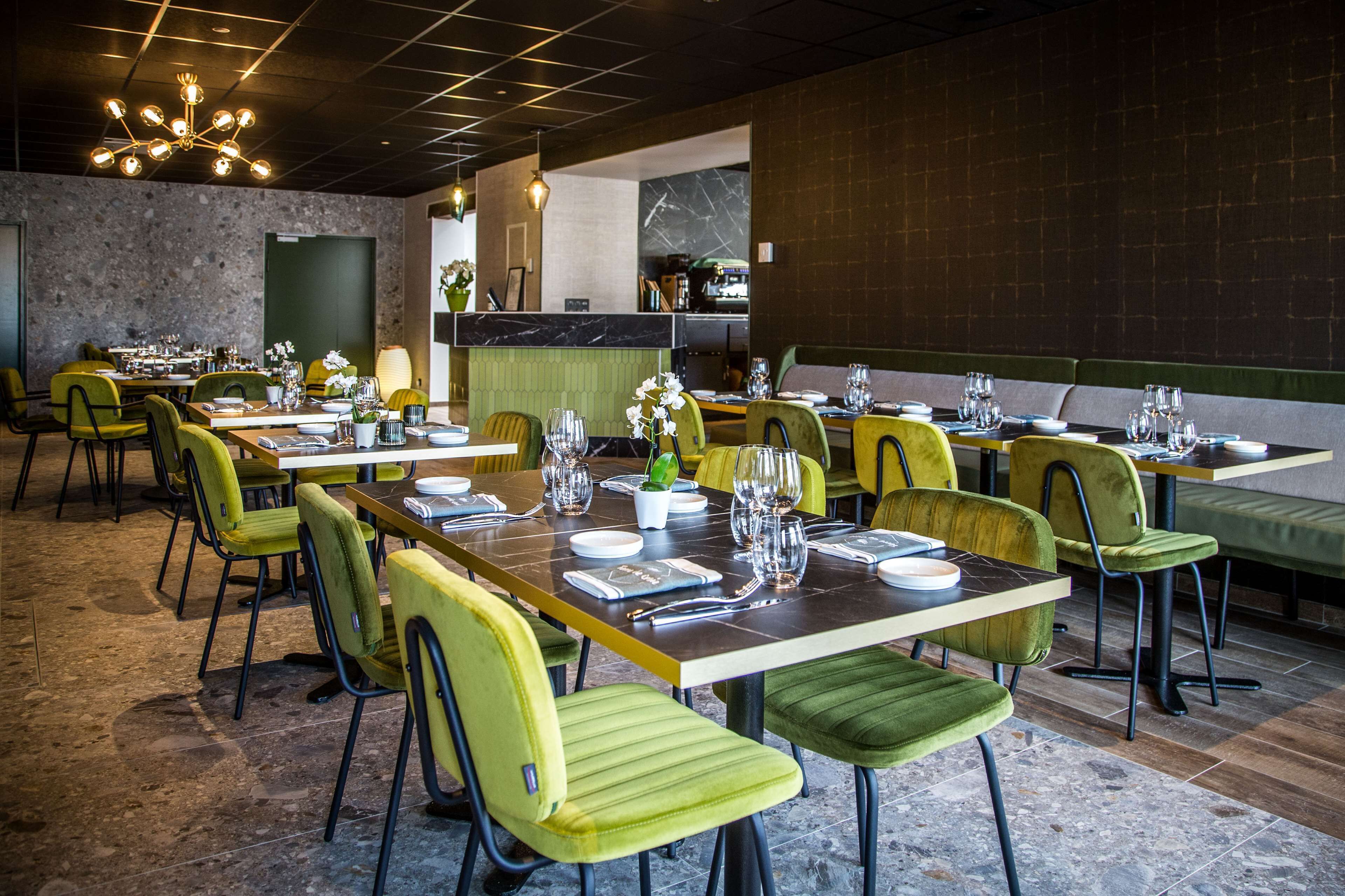 A restaurant with green upholstered chairs, marble-topped tables, and a modern chandelier.