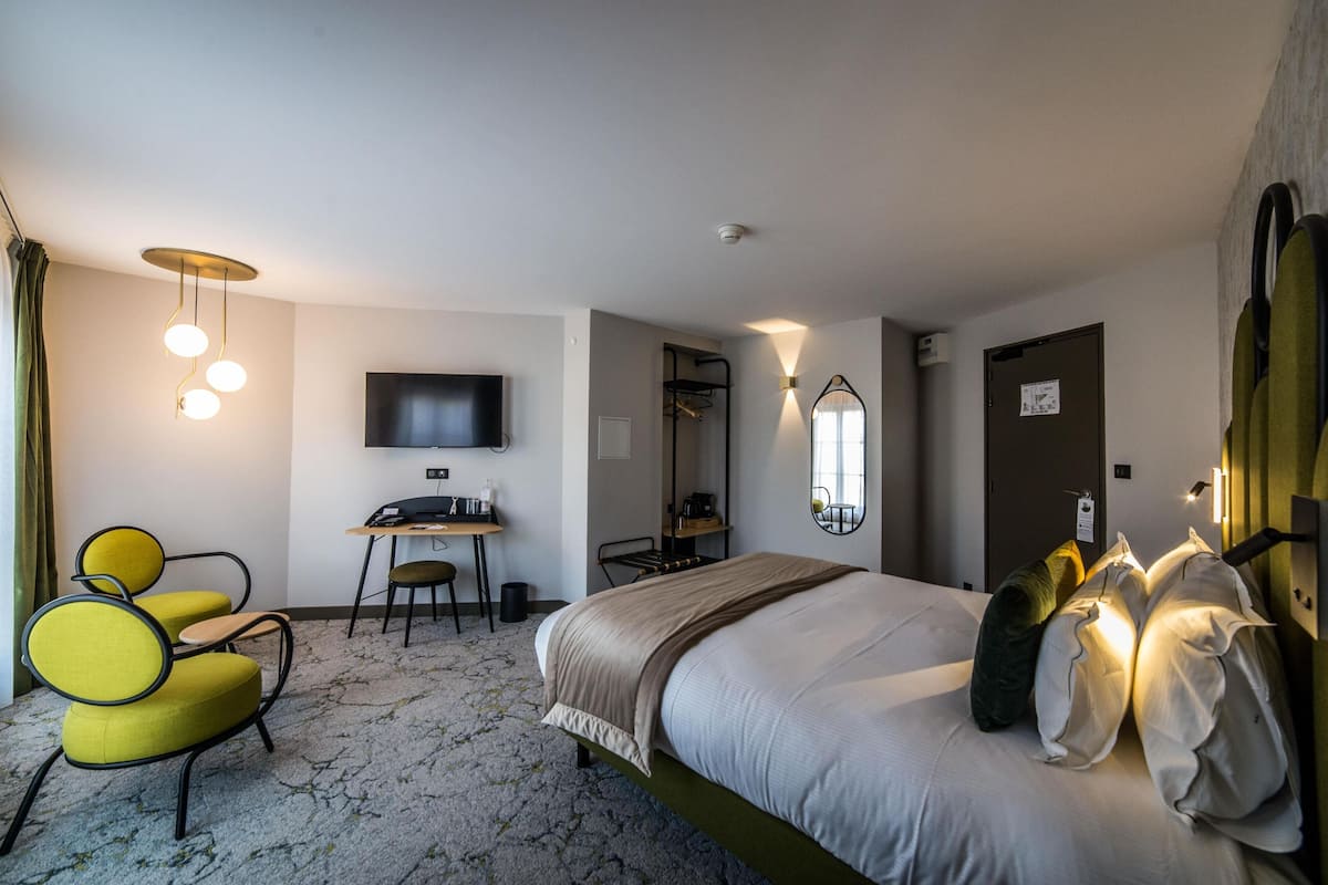 Ein Hotelzimmer mit einem Bett, einem Schreibtisch, einem Sessel, einem Fernseher und einem Spiegel.