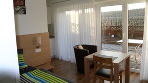 A compact room with a bed, a wooden table, a chair, and a window with a view of a garden.