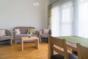 Moderni olohuone, jossa on kaksi harmaata sohvaa, puinen sohvapöytä ja ruokapöytä tuoleineen.