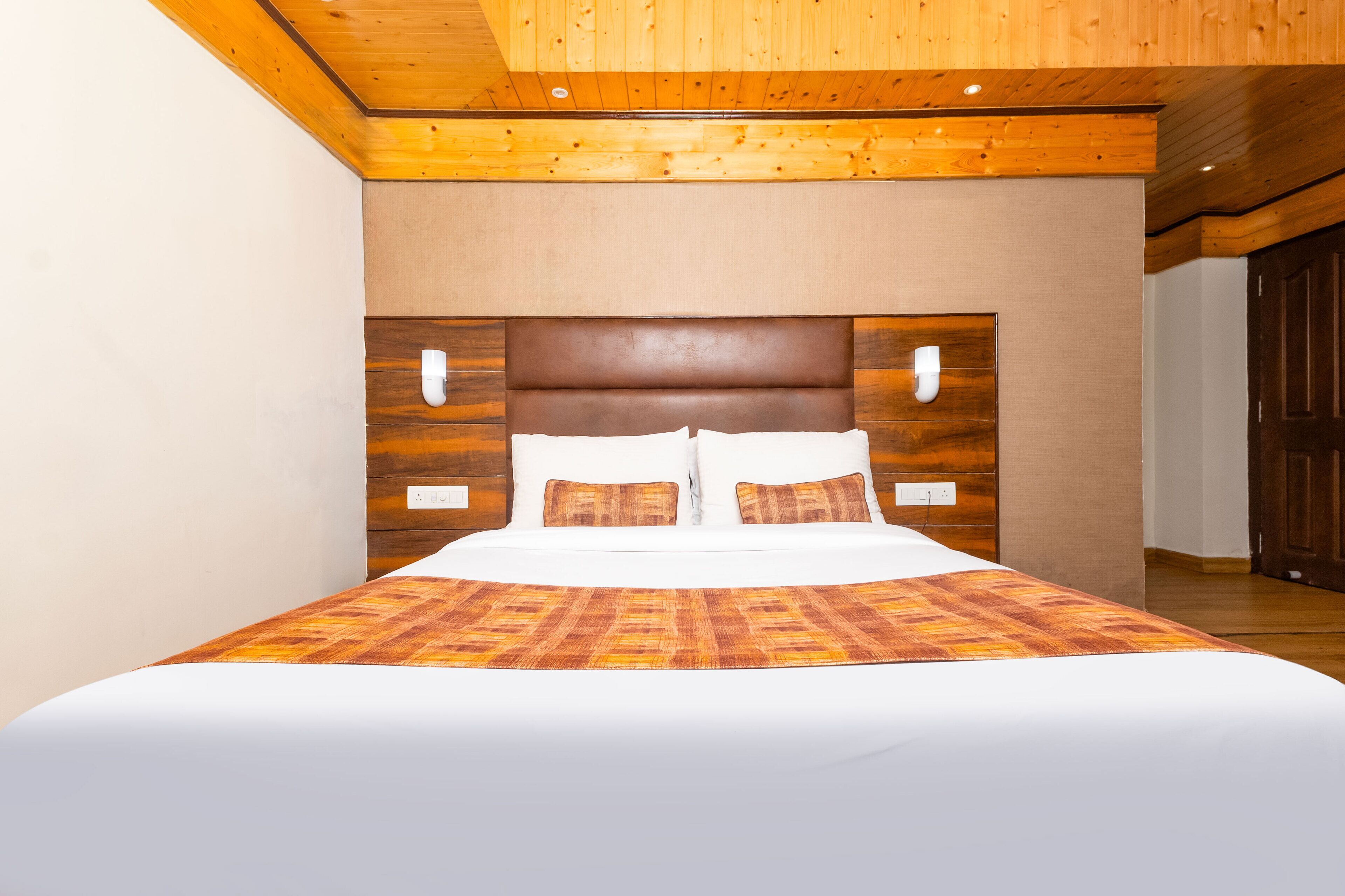 A bedroom with a wooden ceiling, a large bed with a patterned bedspread, and a headboard with wall-mounted lights.