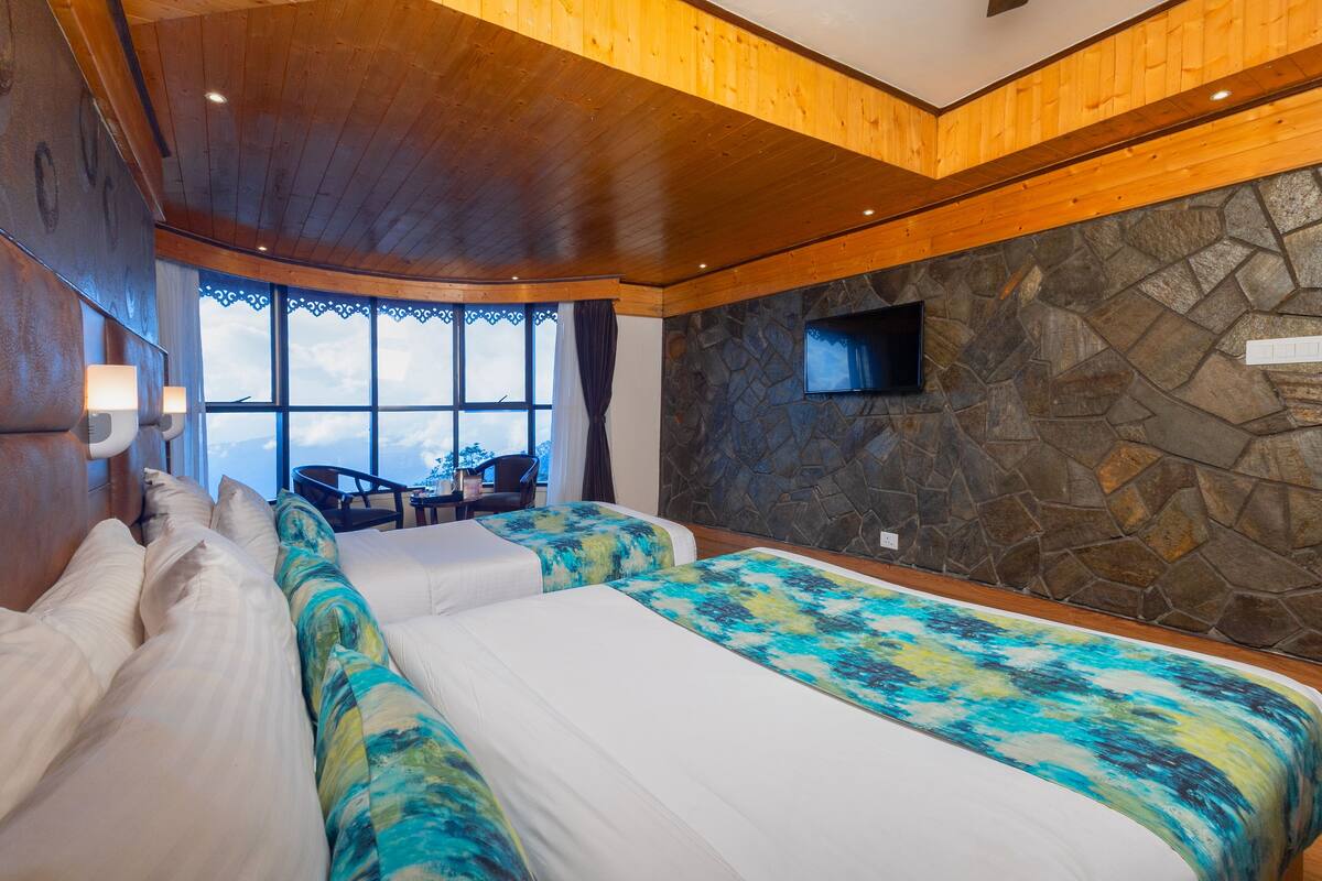 A bedroom with two beds, a stone wall, a TV, and a view of the sky.