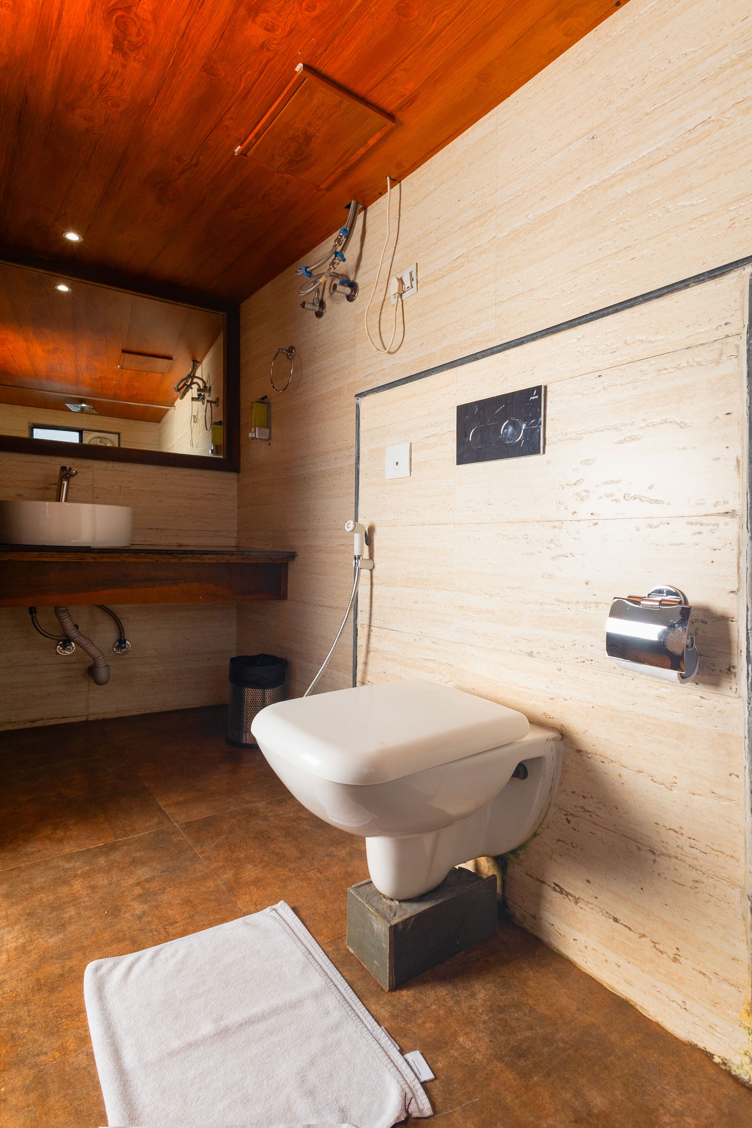 A bathroom with a wooden ceiling, a white toilet, a sink, and a towel on the floor.