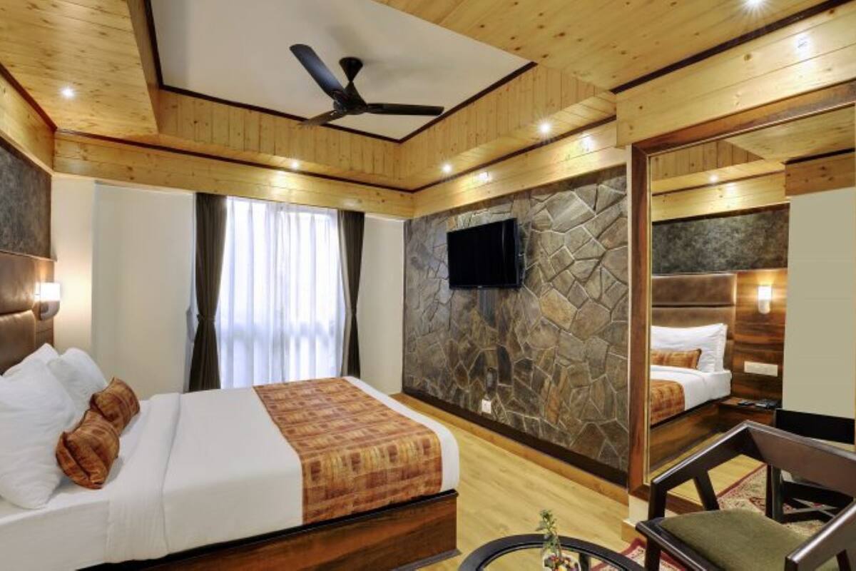 A hotel room with a bed, a television, a ceiling fan, and a large mirror.