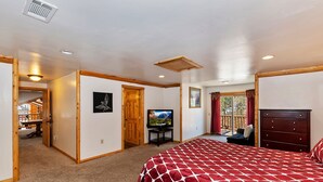 A bedroom with a bed, a television, a dresser, and a window with curtains.