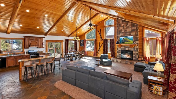 A spacious living area with a fireplace, a large sofa, and a dining area with a kitchen in the background.