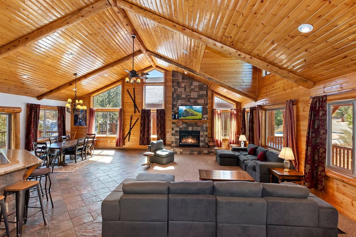 A spacious living area with a fireplace, wooden ceiling, and large windows.