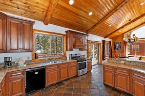 A spacious kitchen with wooden cabinets, granite countertops, a dishwasher, and a stove. - Serenity Now Lodge by Destination Big Bear: Luxury Log Home in Castle Glen Estates! Hot Tub! Pool Table! Ping Pong! (Big Bear Lake)