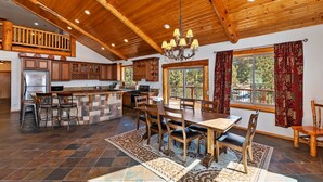 A spacious kitchen with a stone island, wooden ceiling, and a dining area with a large table and chairs.