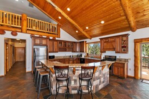 A spacious kitchen with a large island, wooden ceiling, and a view to the outside. - Serenity Now Lodge by Destination Big Bear: Luxury Log Home in Castle Glen Estates! Hot Tub! Pool Table! Ping Pong! (Big Bear Lake)