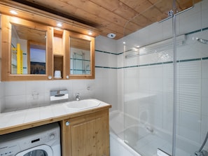 A modern bathroom with a wooden vanity, a glass shower enclosure, and a built-in washing machine.