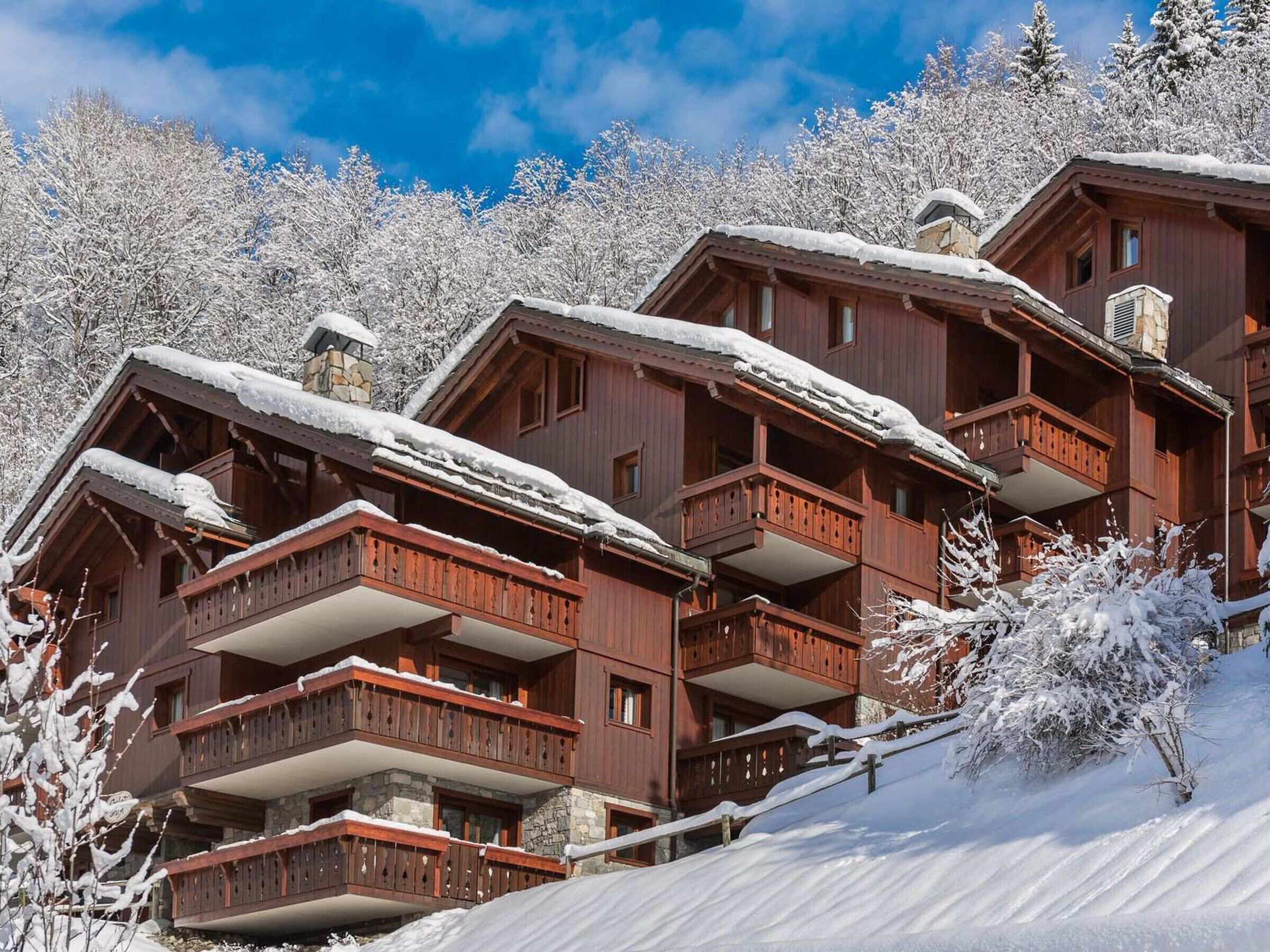 Ein mehrstöckiges Holzchalet mit Balkonen, umgeben von schneebedeckten Bäumen.