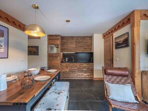 Una cocina moderna con armarios de madera, un comedor con banco, y una zona de estar con una silla acolchada.