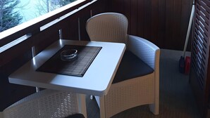 A balcony with a table and chair, a view of buildings and trees, and a wooden wall. - Apartment 'Annabelle' with Shared Garden, Wi-Fi, and Optional Private Pool Use (Lana)