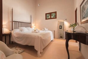 A hotel room with a four-poster bed, a bedside table with a lamp, a small mirror, and a vase with flowers.