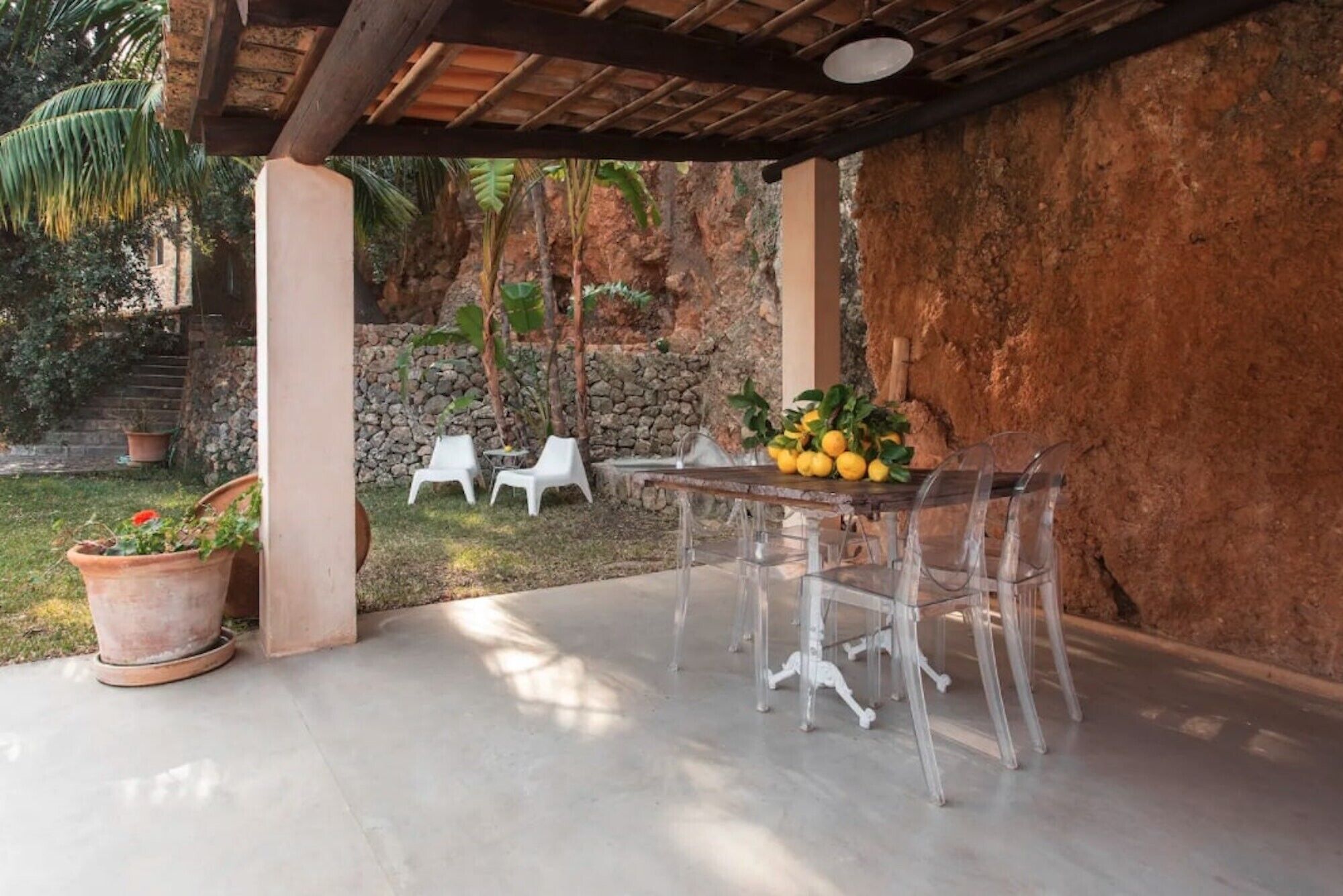 An outdoor patio with a table and chairs, surrounded by a stone wall and greenery.