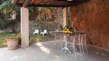 An outdoor patio with a table and chairs, surrounded by a stone wall and greenery.