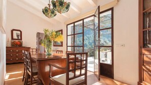 Zona pranzo con tavolo e sedie in legno, un vaso con fiori e vista attraverso ampie finestre.