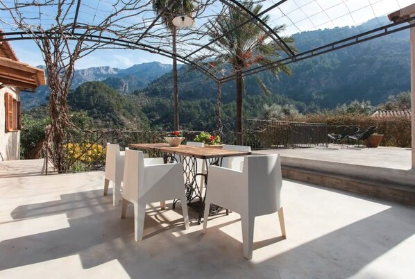A terrace with a table and chairs, a potted plant, and a view of mountains.