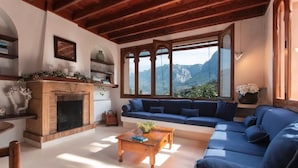 Un soggiorno con camino, un divano blu, un tavolino in legno e vista sulle montagne attraverso ampie finestre.