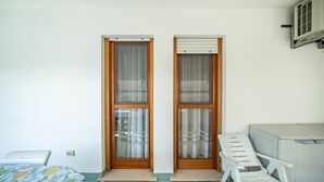 Una habitación con cama, ventana con cortinas, una silla y una mesita.
