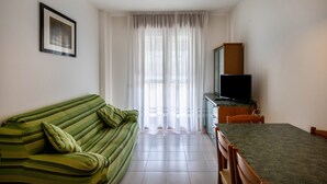 Una habitación con un sofá verde, un televisor sobre un mueble, una mesa de comedor y un ventanal con cortinas.