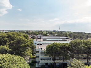 A multi-story building with a flat roof, surrounded by dense greenery and a clear sky.