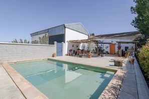 Ein Pool mit Terrassenbereich, ein weißes Gebäude mit Metalldach und eine Backsteinmauer.