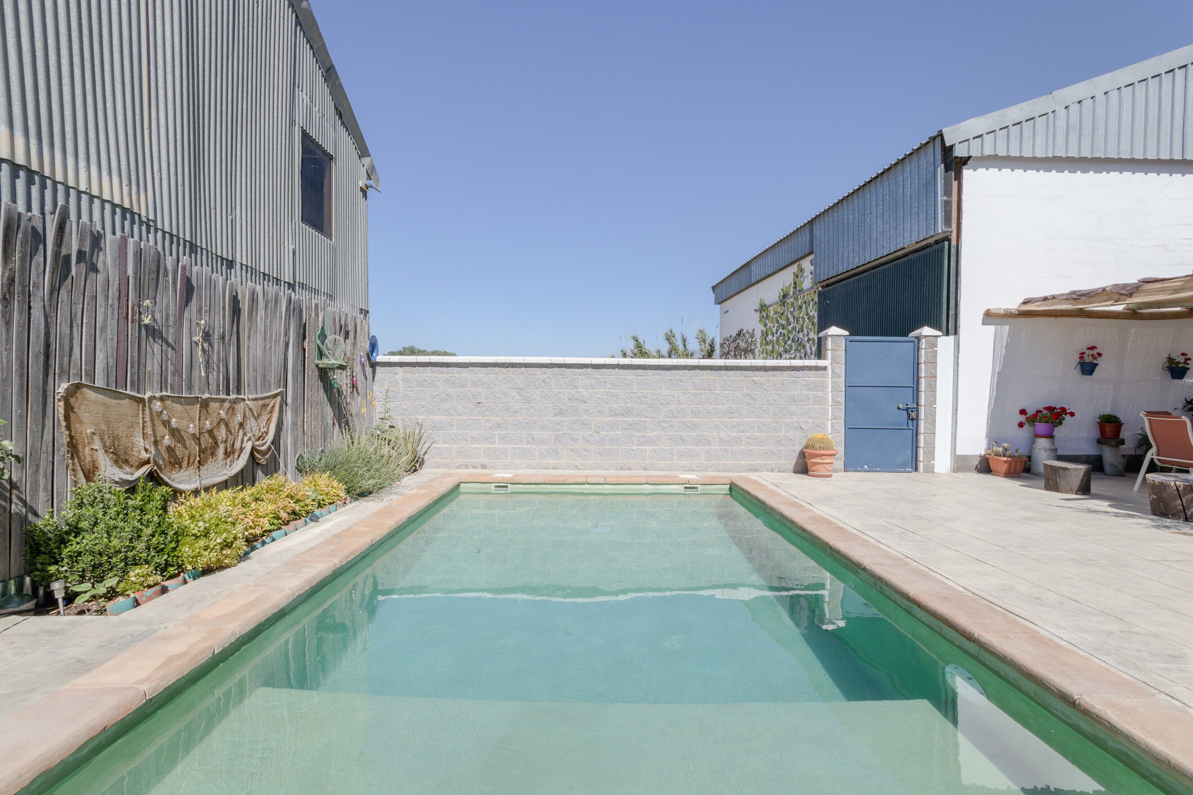 Une piscine rectangulaire avec une plage carrelée, entourée d’une clôture en bois et d’un mur en briques.