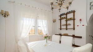Un espace repas comprenant une table, des chaises, un lustre et une étagère murale agrémentée d’objets décoratifs.