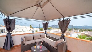 Un espace extérieur aménagé, abrité et doté d’un canapé et d’une table, offrant une vue sur le paysage urbain et les montagnes au loin.