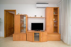 Een woonkamer met een televisie, houten kasten en een deur.
