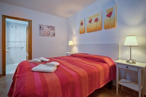 A hotel room with a bed, two bedside lamps, a door leading to a bathroom, and three wall-mounted artworks. - Apartment Coliseo Spaniahome with Balcony, Shared Pool & Wi-Fi (Alfaz del Pi)