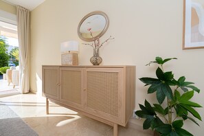 Een houten console met een spiegel, een vaas met bloemen en een potplant.
