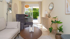 Un salon comprenant un canapé, un fauteuil, une table basse ronde et un meuble sur lequel est posée une plante.