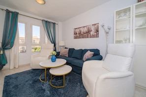 Ein Wohnzimmer mit einer Couch, zwei Sesseln, einem Couchtisch, einer Vase mit Blumen, einer Lampe und einem Bild an der Wand.