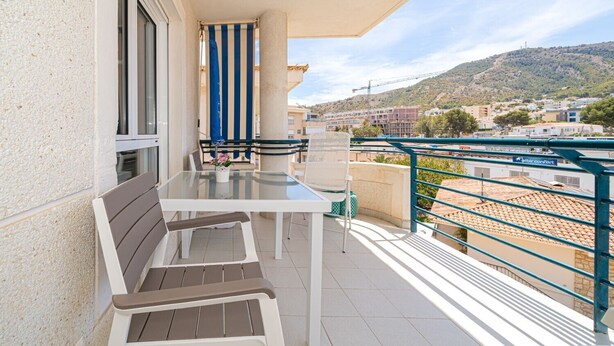 Een balkon met een tafel en stoelen, een gestreept gordijn en uitzicht op een glooiend stadje.