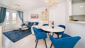 Een moderne woonkamer met een witte bank, blauwe stoelen, een ronde tafel en een kroonluchter.